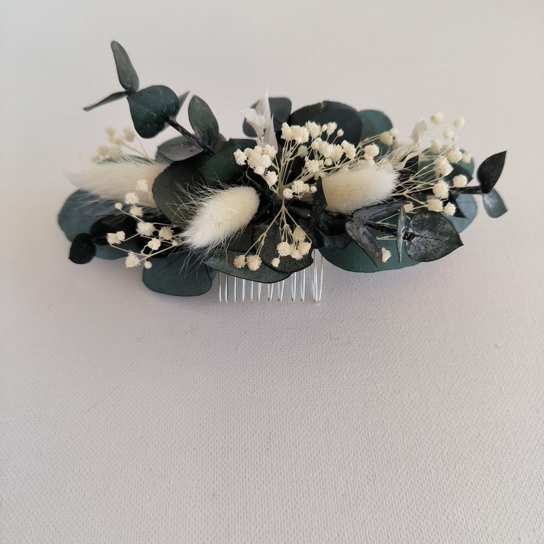 May include: A hair comb with a floral design featuring white dried flowers and dark green eucalyptus leaves.