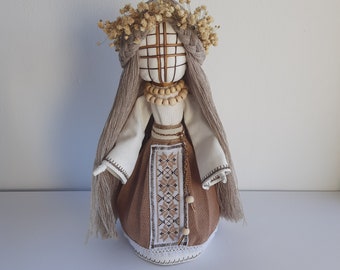 May include: A handmade doll with a white fabric dress, a brown skirt with embroidered details, and a wreath of dried flowers on its head.