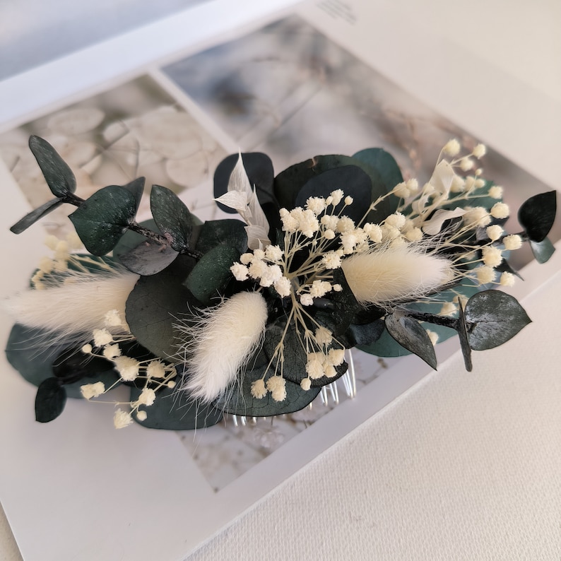 May include: A dark green eucalyptus and white baby's breath hair comb. The comb is decorated with white fluffy pampas grass.