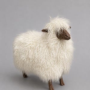 May include: A decorative sheep figurine featuring a dark brown head and legs with a textured, shaggy off-white fleece covering its body. The sheep stands in a profile position, showcasing long, wispy fibres that create a realistic wool appearance.