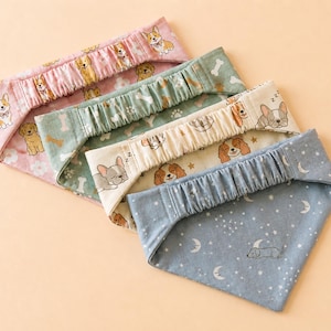May include: Four dog bandanas in pink, green, cream, and blue. Each bandana features a different pattern of dogs, bones, and stars. The bandanas have an elasticated top and a triangular shape.