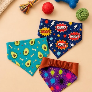 May include: A collection of dog bandanas with playful patterns and phrases, alongside dog toys. The bandanas feature avocado, bone, and comic book-style designs with phrases like "Woof!" and "Bark!" in vibrant colors.