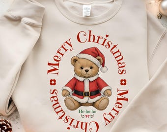 May include: A cream-coloured sweatshirt with a Christmas-themed design. The graphic shows a teddy bear in a Santa Claus outfit, encircled by the words "Merry Christmas" in red. The bear is wearing a red hat and coat with a black belt. The phrase "Ho-ho-ho" is also included.
