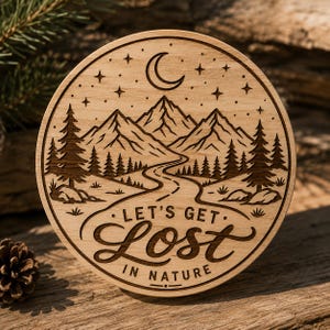 May include: A circular light-colored wooden plaque featuring a laser-engraved mountain landscape with pine trees, a winding road, a crescent moon, and stars. The text "LET'S GET LOST IN NATURE" is engraved in a combination of script and block fonts.