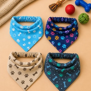 May include: Four dog bandanas in blue, navy, tan, and dark teal, each with a different pattern of paw prints and bones. A rope toy, a red ball, and two other dog toys are also visible.