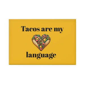 Puede incluir: Un imán rectangular amarillo con el texto "Tacos are my language" en negro. La imagen presenta un diseño en forma de corazón hecho con dos tacos rellenos de varios ingredientes.