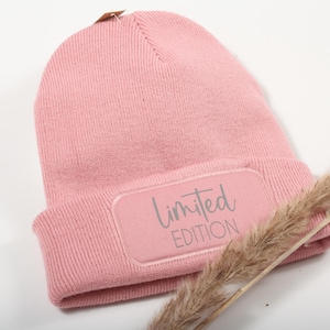 Könnte beinhalten: Eine rosafarbene Strickmütze mit einem grauen Patch, auf dem "Limited Edition" steht.