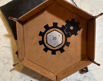 May include: A brown leather dice tray with a black gear design and a silver 20-sided die in the centre. The tray is shaped like a hexagon and has a black leather pouch attached to one side.