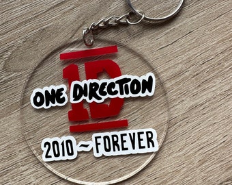 May include: A clear acrylic keychain with a red "1D" logo and the text "One Direction 2010 - Forever".