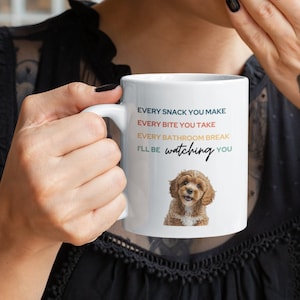 Könnte beinhalten: Eine weiße Keramik-Kaffeetasse mit einer Illustration eines braunen und weißen Hundes und dem Text "Every snack you make, every bite you take, every bathroom break, I'll be watching you".
