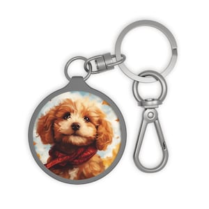 Peut inclure: Un porte-clés rond doté d'un insert circulaire illustrant un chiot au pelage brun doré portant une écharpe rouge. Le chiot est représenté sur un fond de feuilles d'automne. Le porte-clés possède un anneau et un mousqueton en métal argenté.