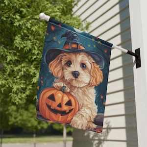 May include: A cute, cream-coloured dog wearing a witch's hat holds a carved orange pumpkin with a jack-o'-lantern face. The dog is surrounded by a dark blue background with stars and a full moon.
