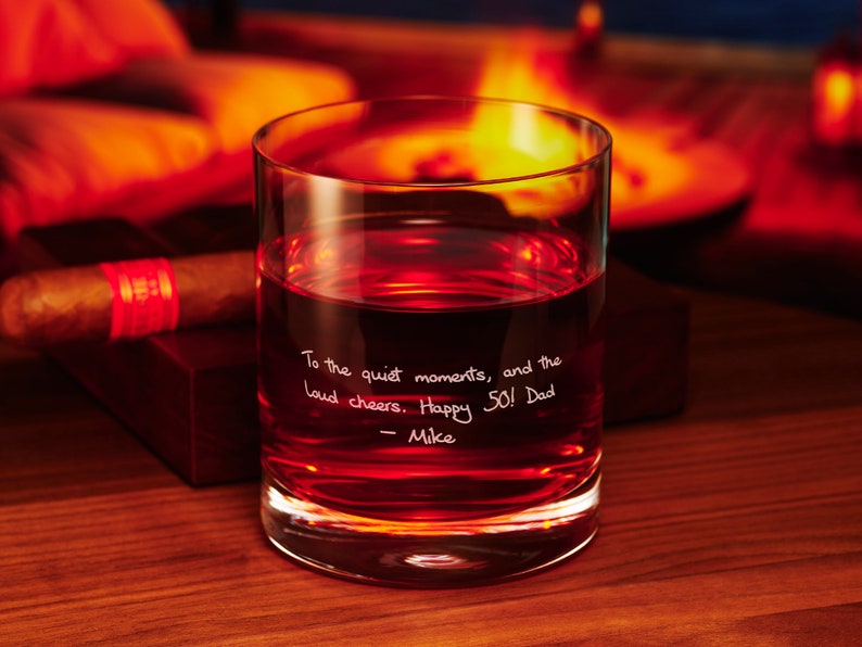 May include: A clear glass tumbler with a handwritten message that reads "To the quiet moments, and the loud cheers. Happy 50! Dad - Mike". The glass is filled with a dark red liquid.