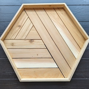 May include: A hexagonal wooden tray with a geometric pattern of light brown wood strips. The tray is made of natural wood and has a rustic look.
