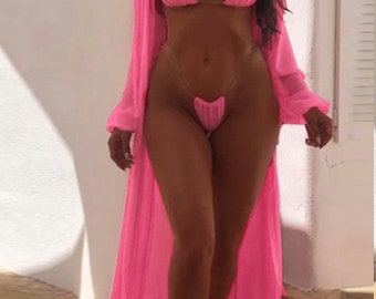 May include: A pink swimsuit with a sheer pink cover-up. The swimsuit has a triangle top and a thong bottom. The cover-up has long sleeves and a long skirt.