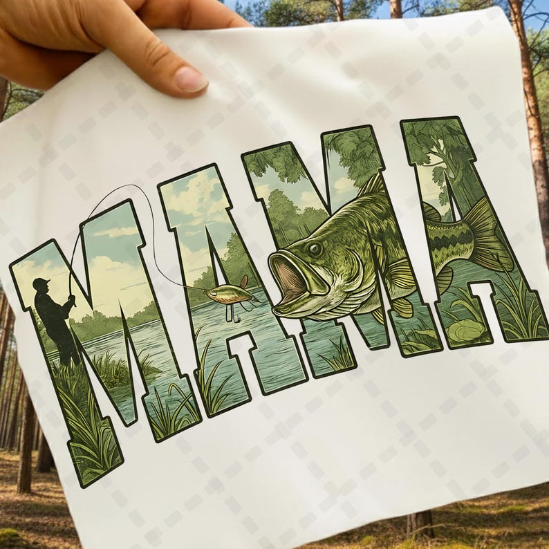 May include: White t-shirt featuring the word "MAMA" in large, green, stylized letters. The letters are filled with a fishing scene, including a fisherman, a fish, and a lake. The shirt is held up by a hand.
