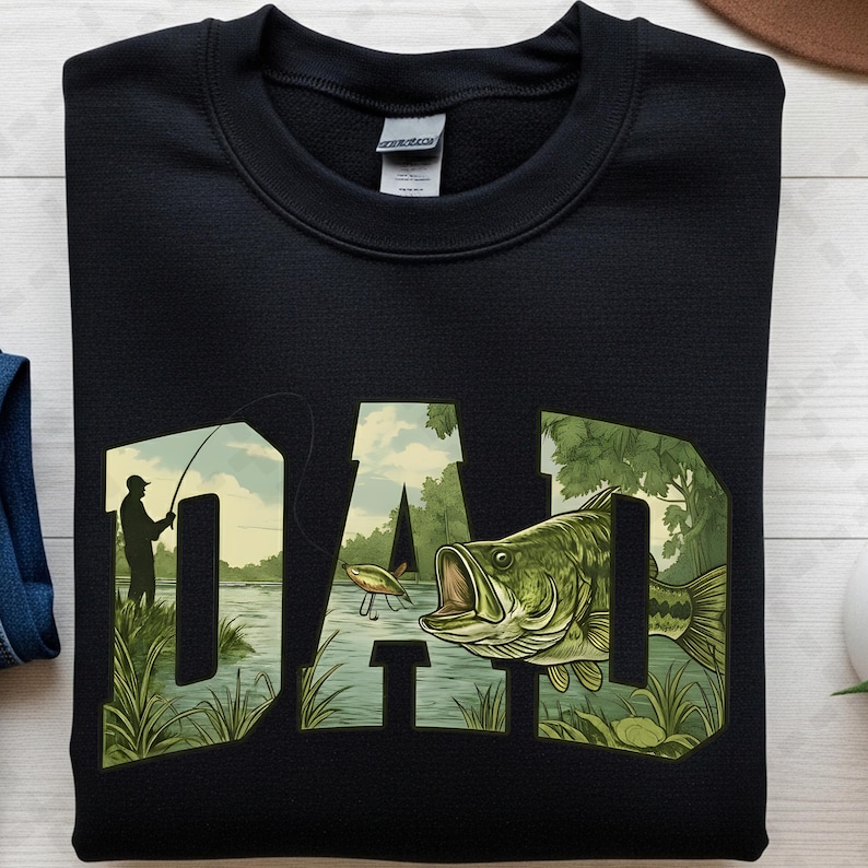May include: Black sweatshirt with the word "DAD" in a green and tan graphic. The "D" features a fisherman, the "A" a lure, and the second "D" a large fish. The sweatshirt is a crew neck.