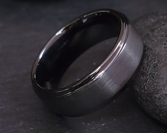 May include: A close-up shot of a dark gray ring with a brushed metal finish. The ring has a polished black interior and a shiny, silver-colored edge. The ring is set against a dark background.