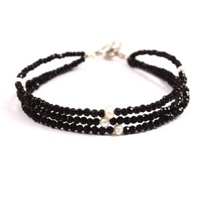 Puede incluir: Un brazalete de ónix negro y perla con tres filas de cuentas de ónix negro y tres perlas blancas.