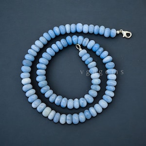 Op de afbeelding: Een lichtblauwe ketting van opaal kralen met een zilveren sluiting. De ketting is gemaakt van ronde kralen en is ongeveer 45 cm lang.