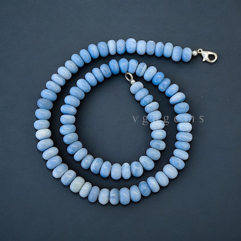 Op de afbeelding: Een lichtblauwe ketting van opaal kralen met een zilveren sluiting. De ketting is gemaakt van ronde kralen en is ongeveer 45 cm lang.