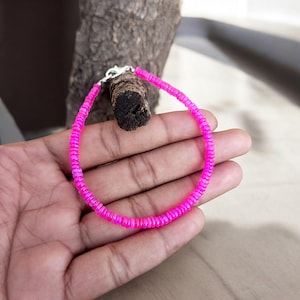 Könnte beinhalten: Ein rosa Perlenarmband mit einem silbernen Verschluss. Das Armband besteht aus kleinen, runden Perlen, die auf einer dünnen Schnur aufgefädelt sind.