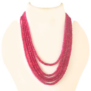 Puede incluir: Un collar de múltiples hilos hecho de cuentas de piedras preciosas facetadas de color rosa. El collar está en capas y cuelga hasta el pecho.