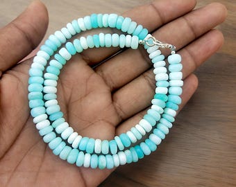 May include: A light blue and white opal bead necklace with a silver clasp. The necklace is made of round beads that are graduated in size, with the larger beads at the center of the necklace and the smaller beads at the ends.