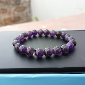 May include: A purple amethyst gemstone bracelet with round beads.