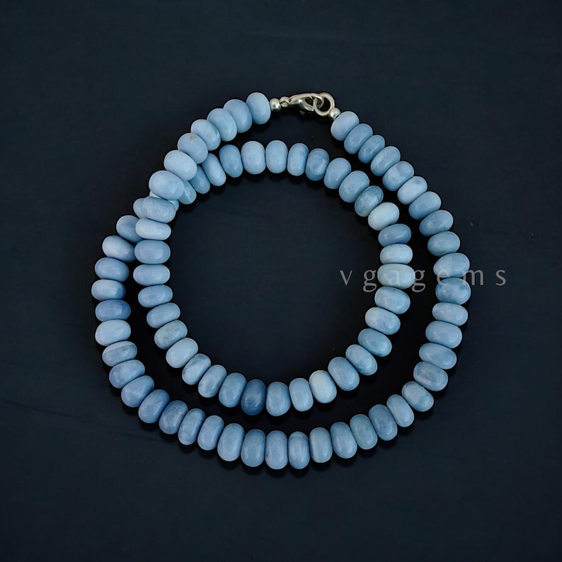 Op de afbeelding: Een lichtblauwe edelsteenketting gemaakt van ronde kralen. De ketting is geregen op een zilveren ketting en heeft een zilveren sluiting.