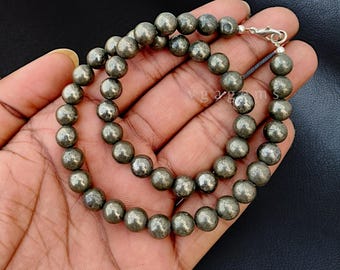 May include: A gold-toned pyrite beaded necklace with a silver clasp. The necklace is made of round beads and is approximately 18 inches long.