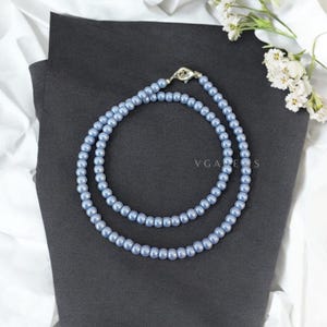 以下が含まれることがあります： 薄い青色の真珠でできた2連ネックレス。ネックレスには銀色の留め具が付いています。