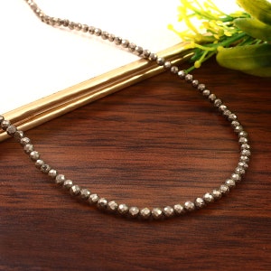 May include: A silver necklace made of small, faceted pyrite beads. The necklace is on a wooden surface.