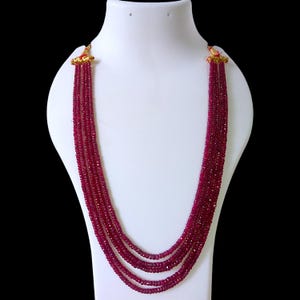 Puede incluir: Un collar de varias hileras hecho de cuentas de rubí rojo. El collar se muestra en un maniquí blanco.