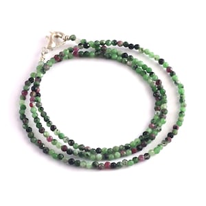 Puede incluir: Un collar de múltiples hilos hecho de cuentas de piedras preciosas verdes, negras y rosas. El collar está hecho de cuentas pequeñas y redondas y tiene un cierre plateado.