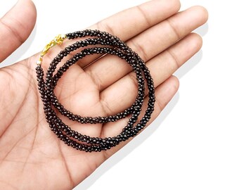 May include: A black beaded necklace with a gold clasp. The necklace is made of small, round beads and is approximately 18 inches long.