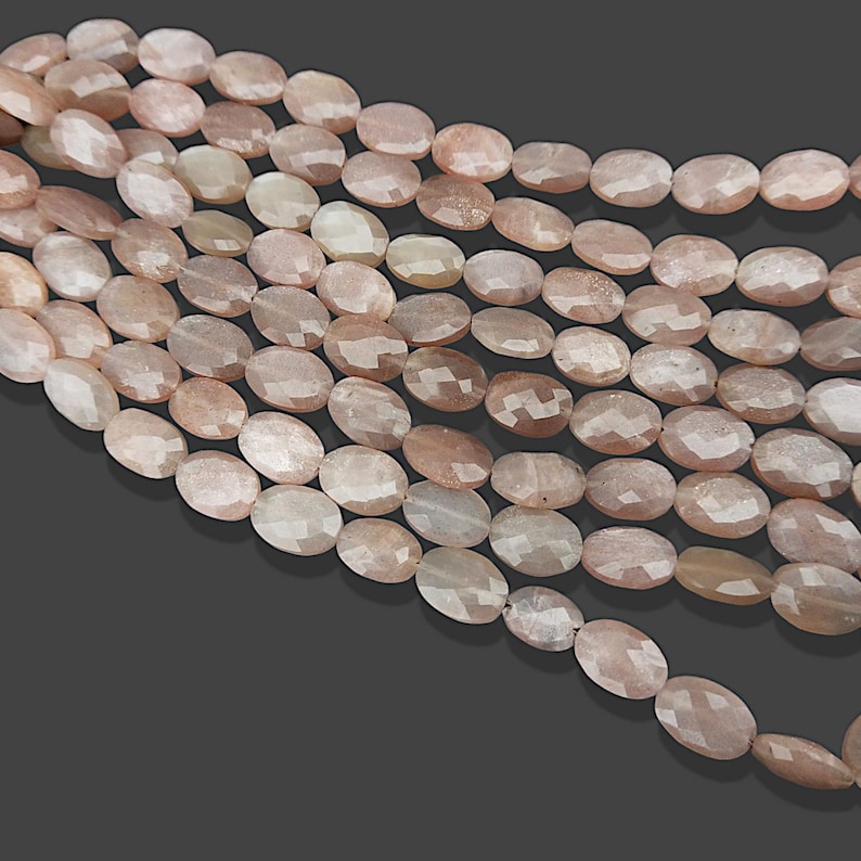 May include: A strand of oval-shaped sunstone beads, each bead is a light peach colour with a shimmery, iridescent finish.