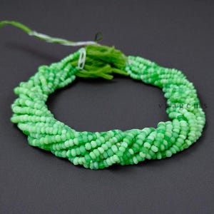 May include: A collection of light green beads, tightly strung together, forming a spiral shape. The beads are a mix of light and medium green shades, with a matte finish. A green tassel and string are visible at the top, suggesting they are ready for use in jewelry making.