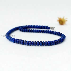 May include: A necklace composed of small, round, deep blue beads. The beads are strung together with a silver clasp. The necklace is displayed on a white surface. The text "vgagems" is visible in the lower left corner.