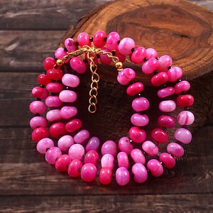 May include: A multi-strand necklace made of pink and white agate beads with black accents. The necklace has a gold clasp.