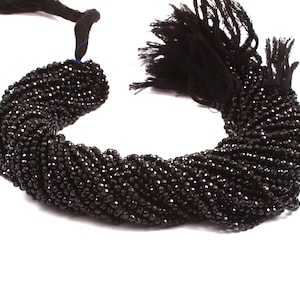Peut inclure: Un brin de perles de pierres précieuses facettées noires. Les perles sont petites et rondes, et elles sont enfilées sur un fil noir. Les perles sont disposées en une spirale lâche.