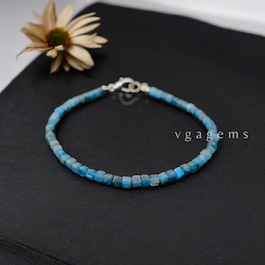 May include: A delicate bracelet featuring small, square, blue gemstones strung together. The bracelet has a silver clasp and is displayed on a black surface. The text "vgagems" is visible in the image.