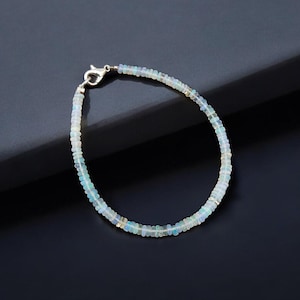 May include: A delicate bracelet made of small, iridescent opal beads. The bracelet is strung on a silver chain and has a silver clasp.