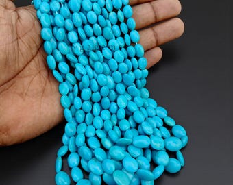 May include: A collection of bright turquoise oval beads. The beads are a vibrant, solid colour and appear to be strung together. The beads are held in a hand against a dark background.