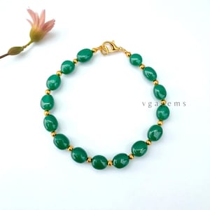 May include: A green beaded bracelet with gold-colored accents and a clasp. The oval-shaped beads are a vibrant green color, and the bracelet is strung with small gold-colored beads. The text "vgagems" is visible on the right side.