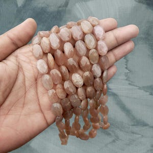 May include: A strand of oval-shaped sunstone beads with a faceted finish. The beads are a light peach colour with a subtle shimmer.