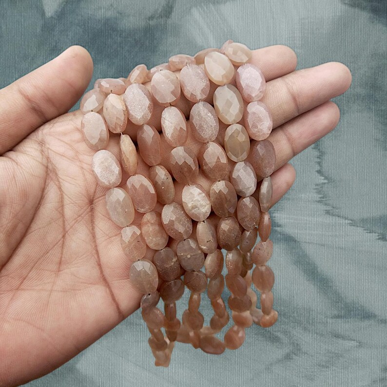 May include: A strand of oval-shaped sunstone beads with a faceted finish. The beads are a light peach colour with a subtle shimmer.