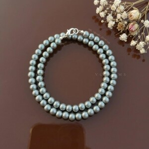 May include: A double-strand necklace composed of uniform, round, metallic grey beads. The necklace features a silver-toned lobster claw clasp and is arranged in a circular shape. The beads have a smooth, reflective surface finish throughout.