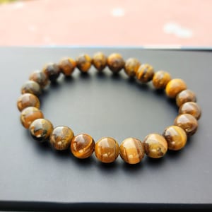 May include: A brown and gold tiger's eye beaded bracelet. The bracelet is made of round beads and is strung on a clear elastic cord.