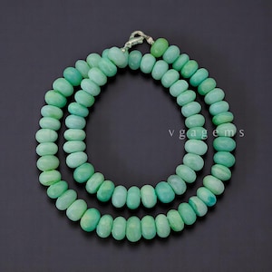 May include: A necklace composed of two strands of light green, oval-shaped beads. The beads are strung together with a silver clasp. The background is a solid black.